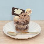 Dinosaur-themed chocolate dessert cup with layered cream and a white chocolate piece on a white plate.